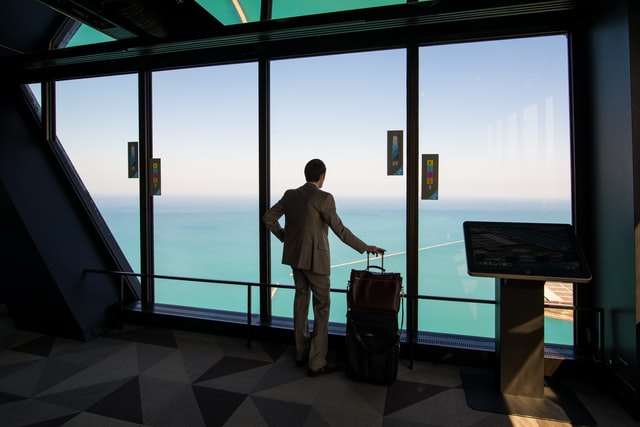 Man with luggages looks through the window in an airport (Business Travel Tips)