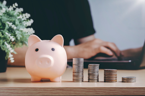 Saving money wealth and financial concept. Asian men working at home during the crisis are calculate family income and expenses, along with pension coins and piggy banks on wooden floors.